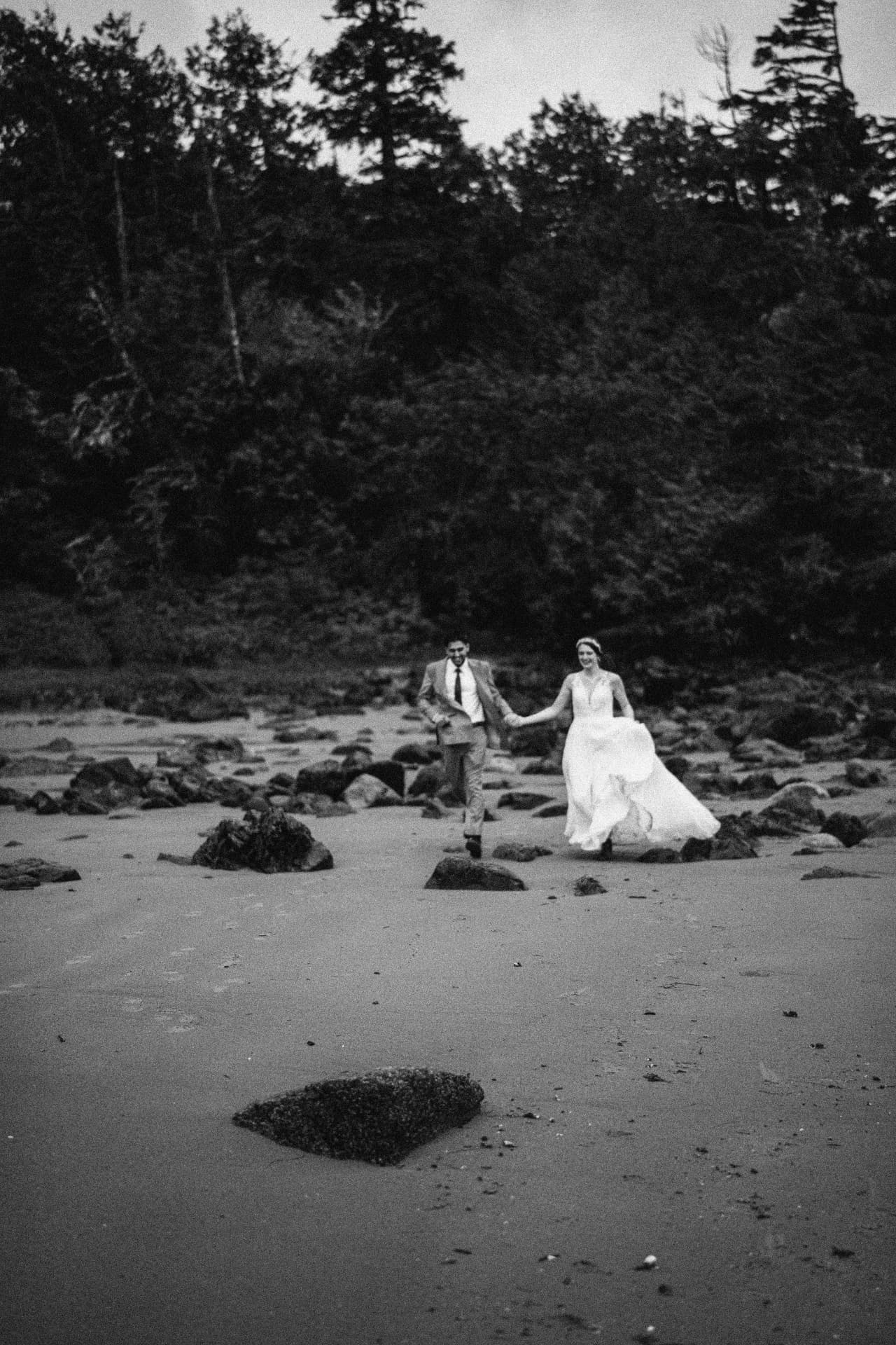 Newlyweds running hand in hand along a rocky Pacific beach